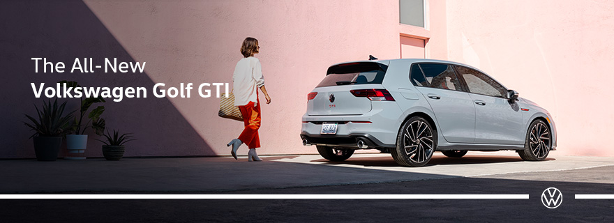 Person walking toward a white Volkswagen Golf GTI parked against a pink wall.