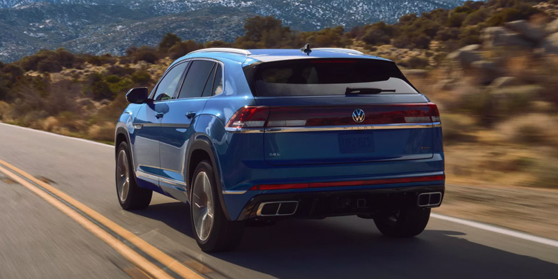 Blue Volkswagen Atlas Cross Sport driving on a scenic mountain highway with rear view in motion.
