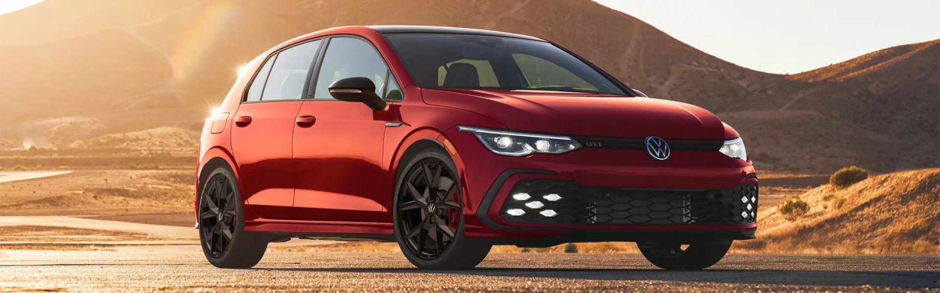 Red Volkswagen GTI driving on a road.