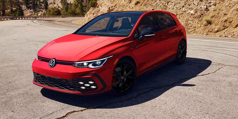 Red 2026 Volkswagen GTI hatchback driving on a road.
