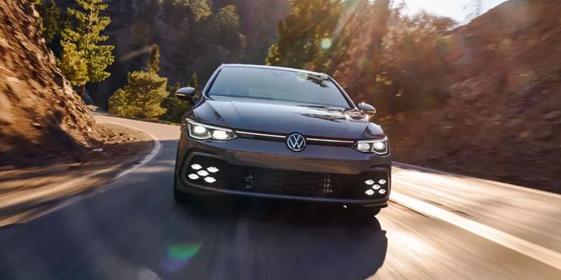 Front view of a Volkswagen GTI driving on a curving road.