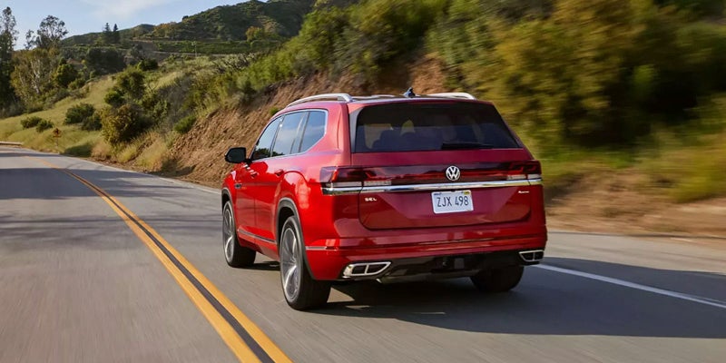 Red 2026 Volkswagen Atlas rear three-quarter view driving on a winding road.