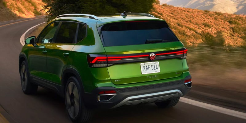 Rear view of a green 2026 Volkswagen Taos SUV driving on a road.